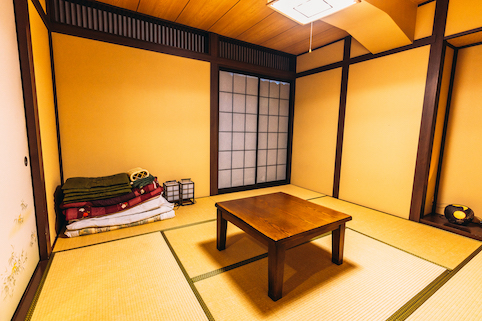 和室の真ん中に木製の机があり、隅に布団が畳まれています